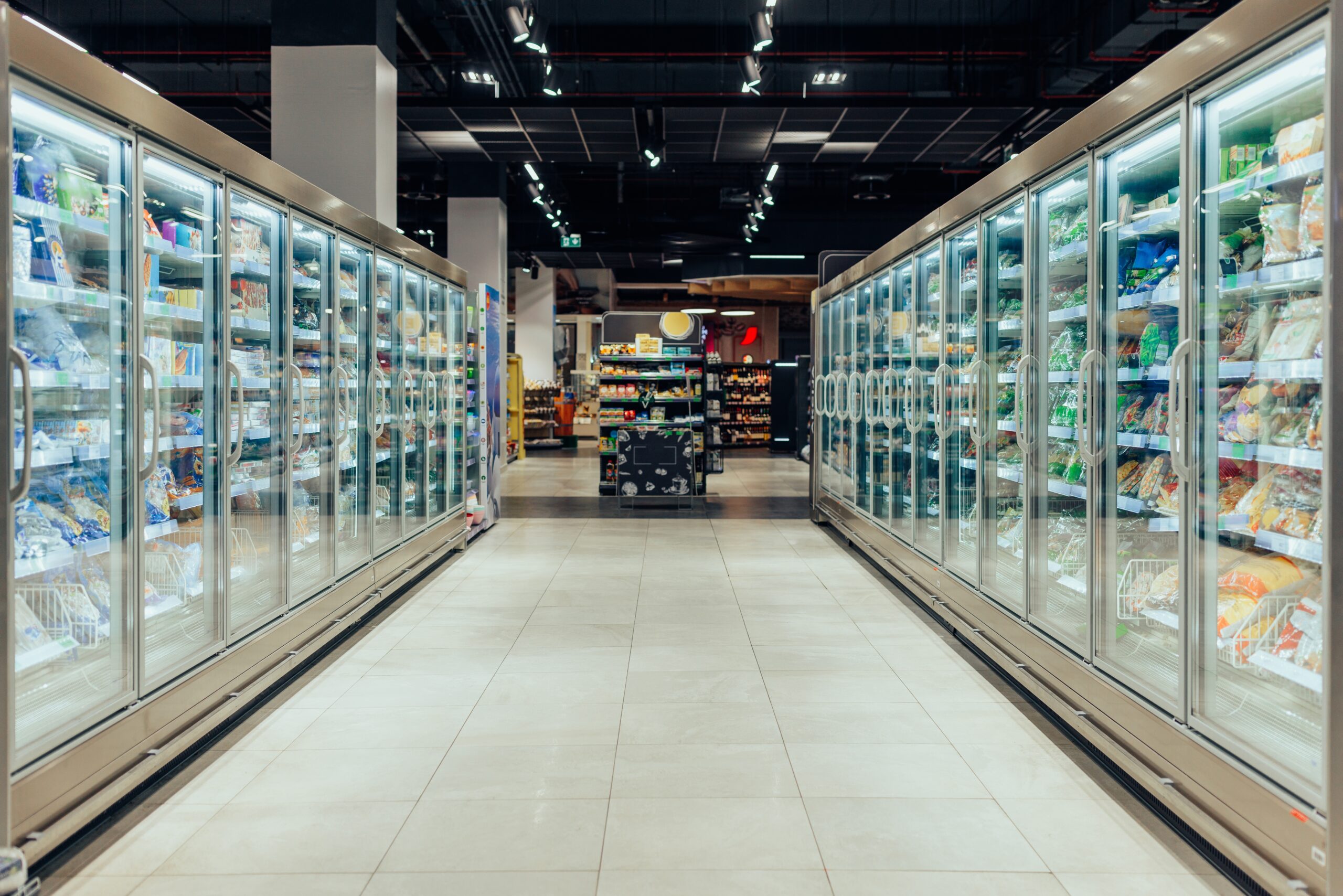 Empty,Supermarket,Aisle,With,Freezers,Showcases,With,Different,Products Aisle with refrigerated shelves filled with various products in a well-lit grocery store.